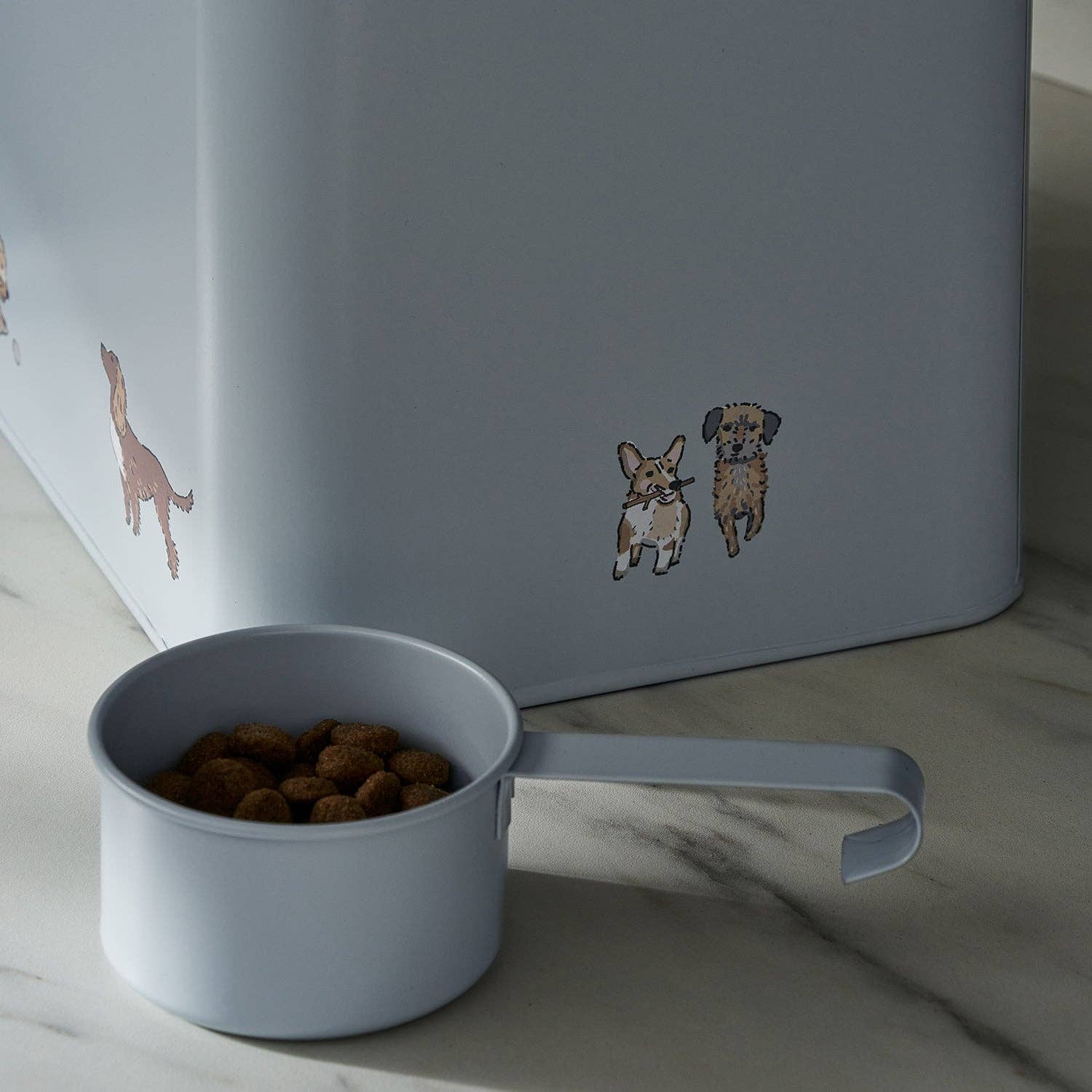 Gray bowl with dog food next to a gray container with dog illustrations on a marble surface