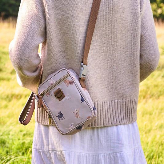 Person holding a patterned crossbody bag in a grassy field