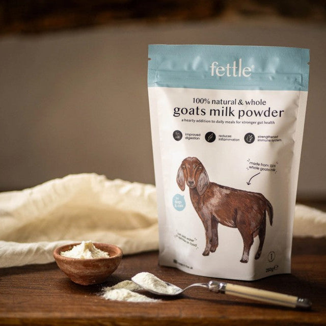 Fettle goats milk powder package on a wooden surface with a bowl of powder and a spoon.