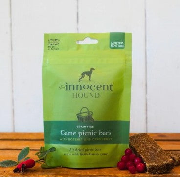 Green package of 'The Innocent Hound' game picnic bars on a wooden surface with berries.