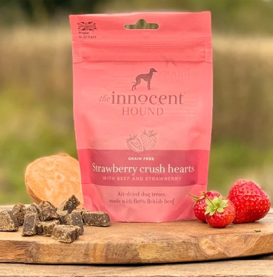 Pink package of 'The Innocent Hound' dog treats with strawberries and a treat on a wooden surface.