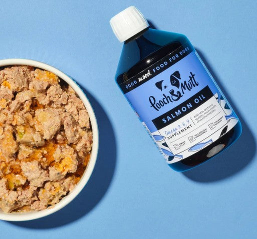 Bottle of Pooch & Mutt salmon oil supplement next to a bowl of dog food on a blue background